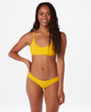 Woman with brown hair against white background wearing a bright yellow bikini.