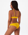 Woman with brown hair against white background wearing a bright yellow bikini.